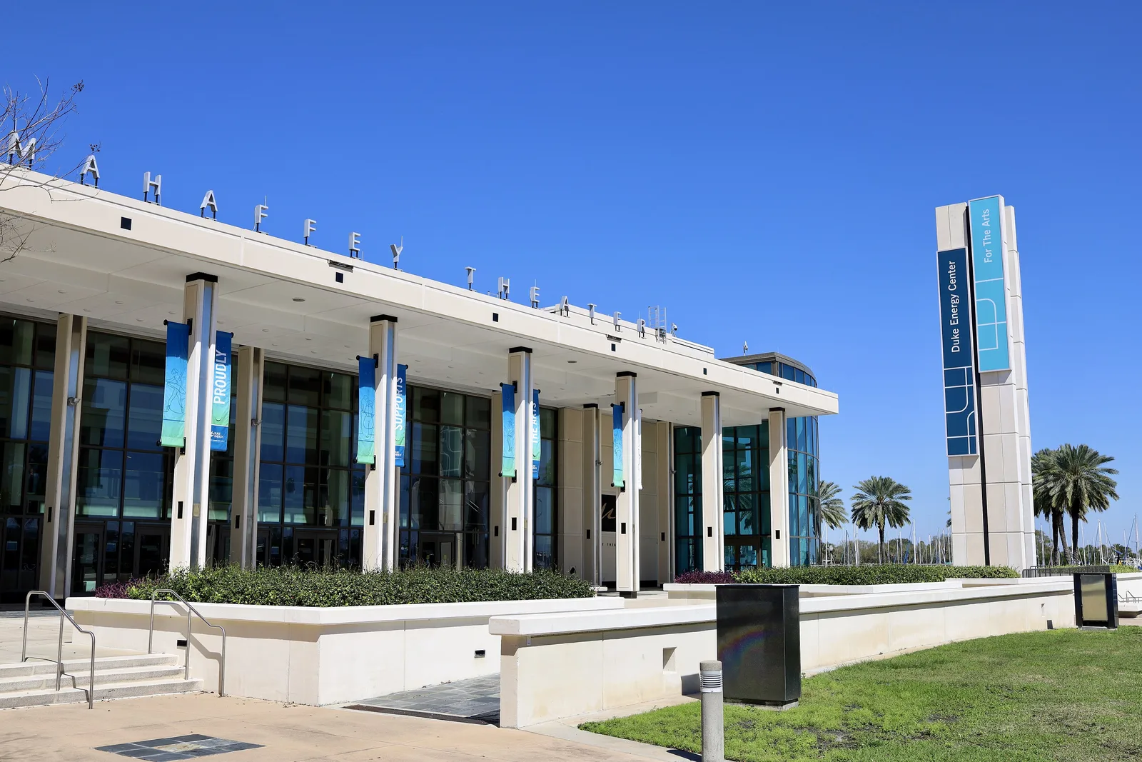 The glass front and colonnade of the Mahaffey Theater on the downtown St. Petersburg waterfront under a clear sky.