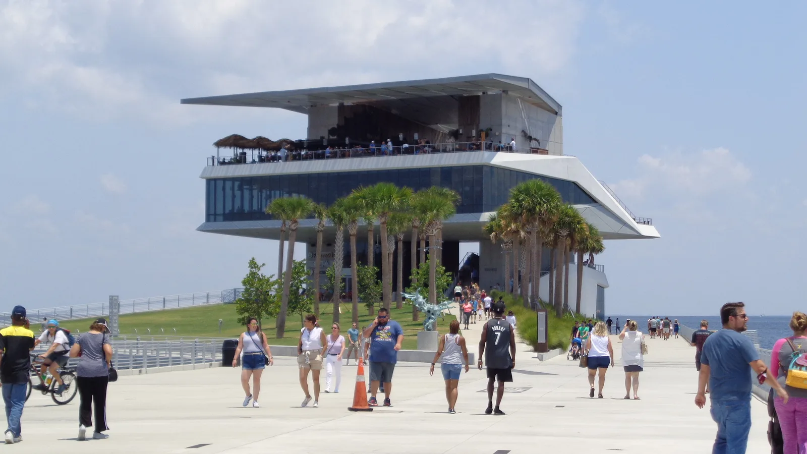 People stroll the wide walkway of the St. Pete Pier toward Pier Point on a sunny day.