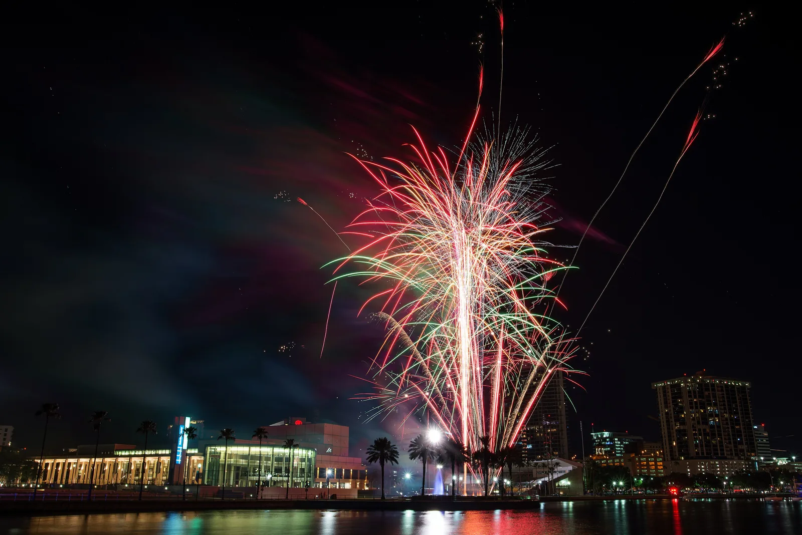 Fireworks burst over the downtown St. Petersburg waterfront beside the Mahaffey Theater, seen across the water from the south.